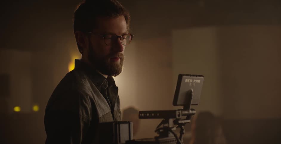 A man with glasses and a beard watches a screen