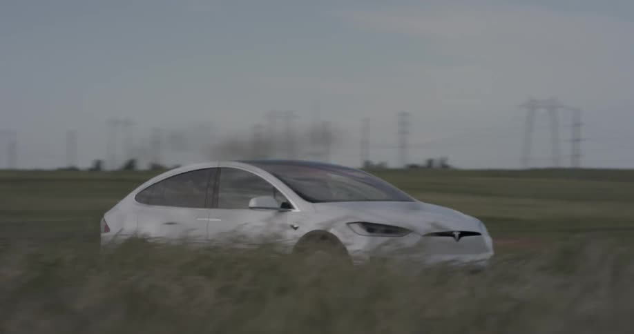 A car that is driving through a field with windmills