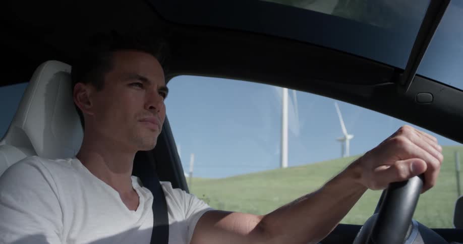 Man Driving Electric Car Through Wind Farm