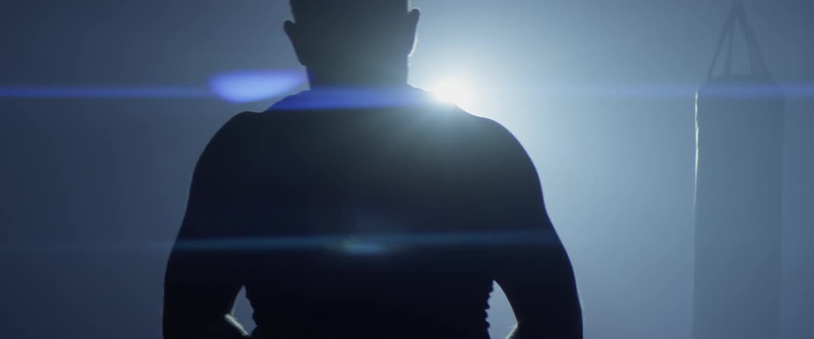 A man walks until he blocks out the light with his body then takes something from his shoulders