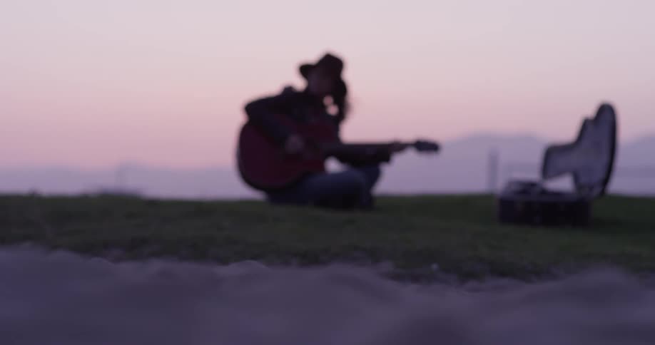 Woman sits on a hill in the country and plays a guitar