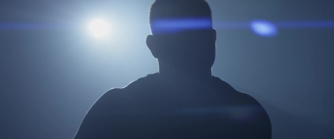 A muscular man walks through a dark room then takes a jump rope off his shoulders