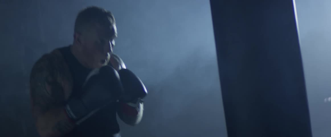 Man wearing a tank top punching boxing bag with gloves