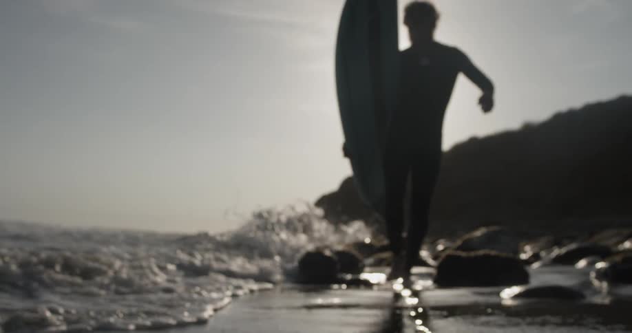 A man walks across the beach with the waves hitting his feet