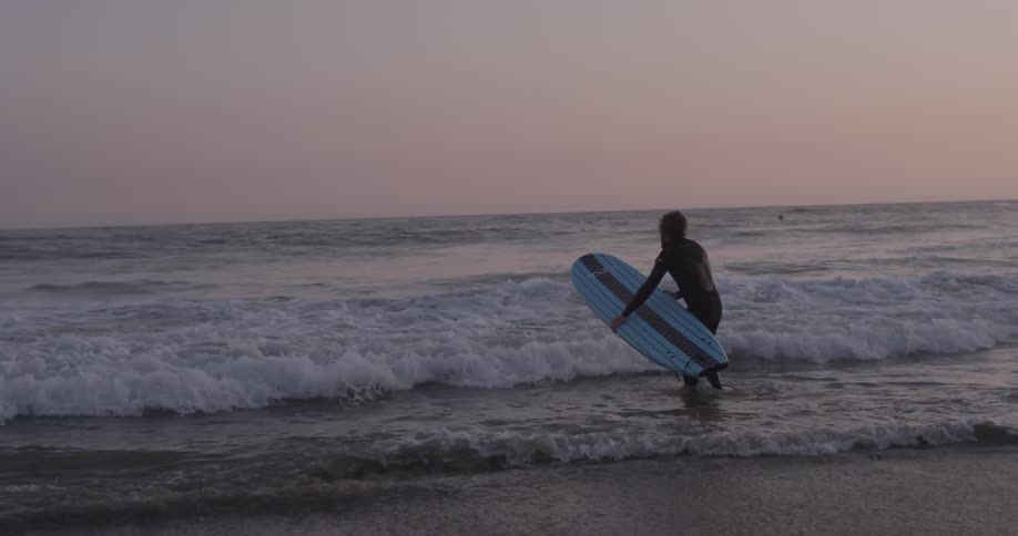 A man is walking to the ocean and holding a surfboard