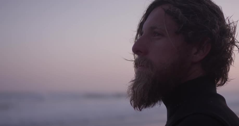 A man in a wetsuit looking at the sea at sunset