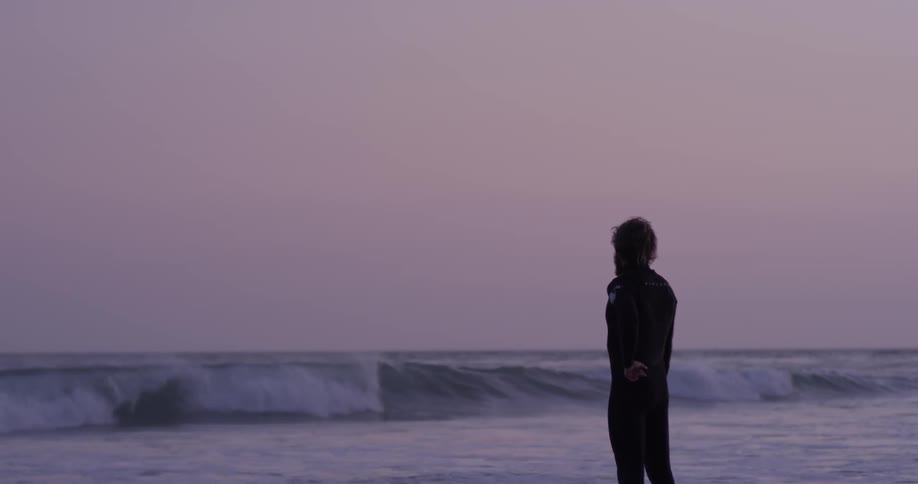 A man looks out at the ocean as waves roll toward him