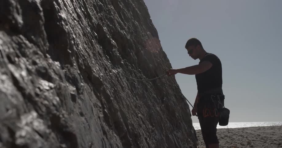 Man connects rope harness as he prepares to climb cliff