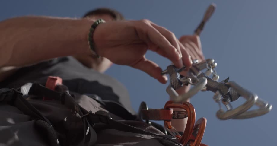 A man grabs a few of his rock climbing equipment and attaches them to places on his body