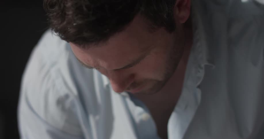 A man wearing a white shirt looking down at something on a desk