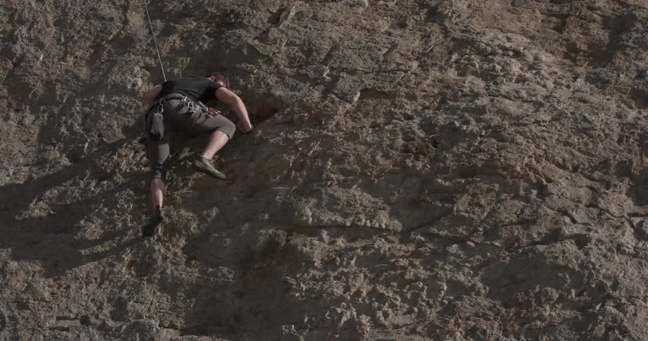 A man in grey shorts climbing up a rock wall