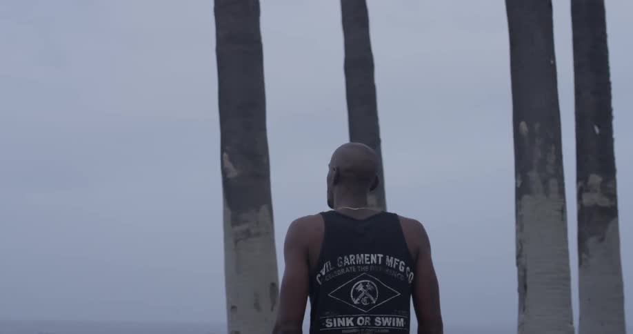 A man is walking on the beach toward some trees and grabs one