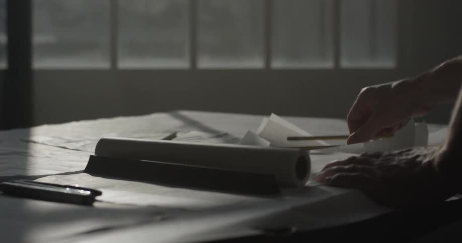 A man that is sketching a blueprint on a desk