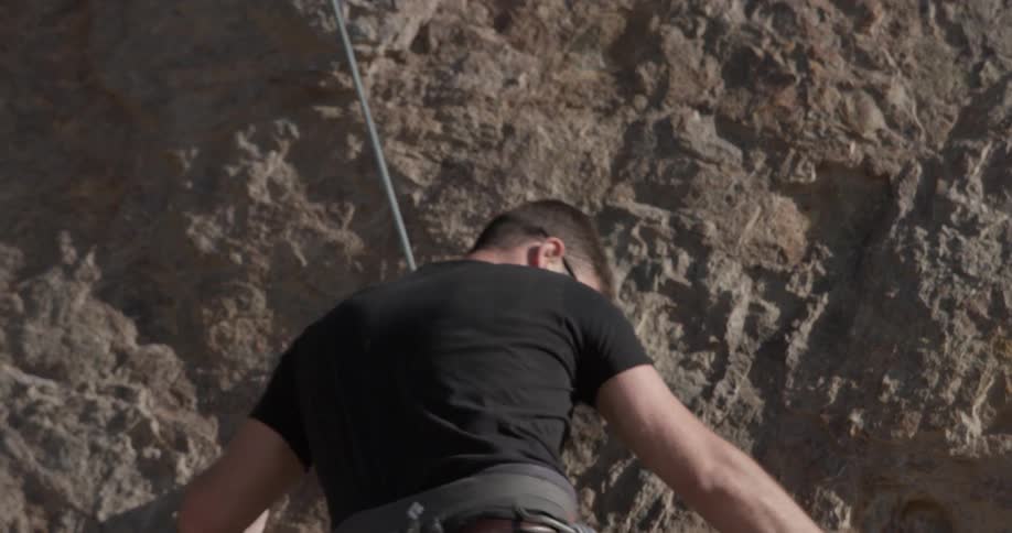 A man looks up and down as he climbs a cliff