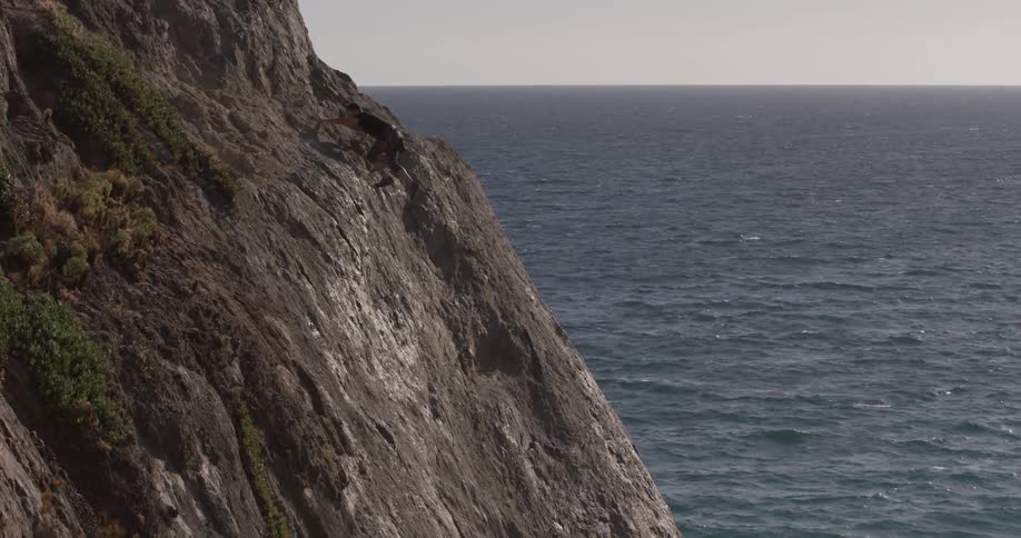 A man climbing up a large cliff beside the ocean