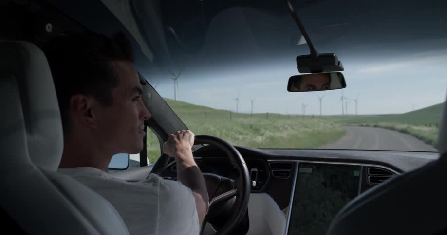 A man driving a car down a dirt road next to some fields