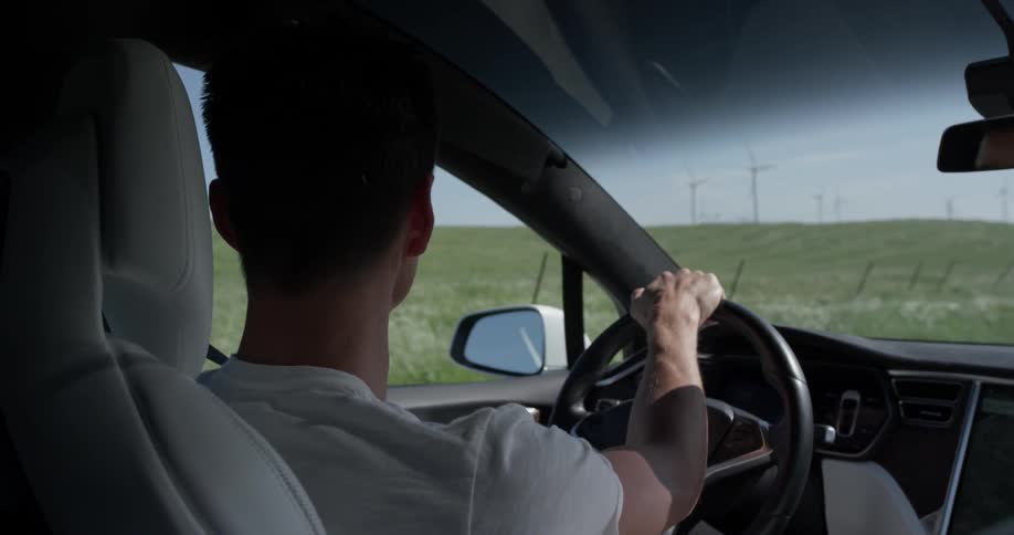 A man that is driving a car between some fields