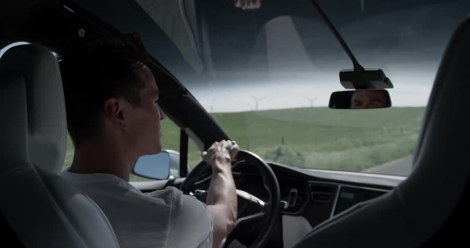 Man Driving Electric Car Through Wind Farm