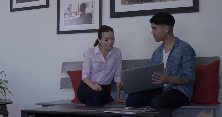 A man shows a woman something on the screen of a laptop