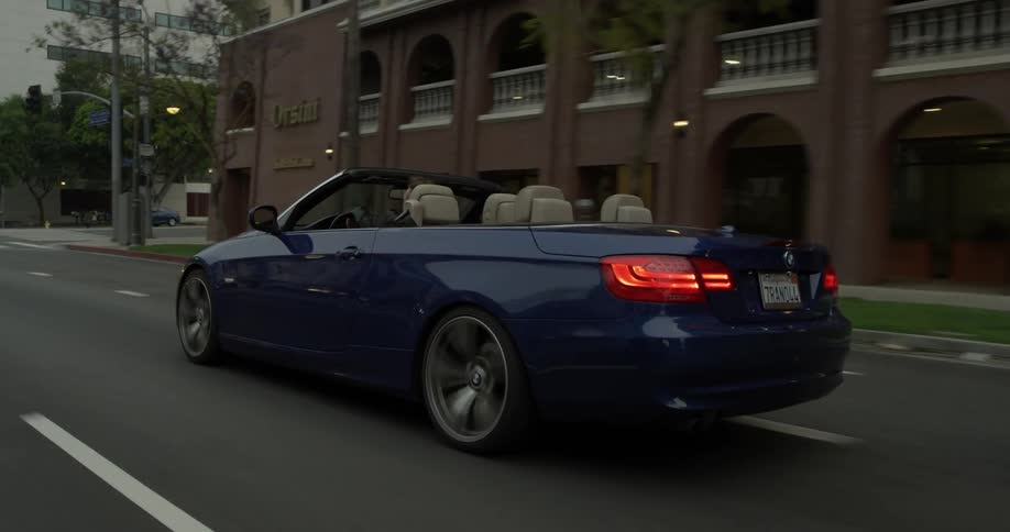 A blue convertible cruises down the city street as evening comes closer