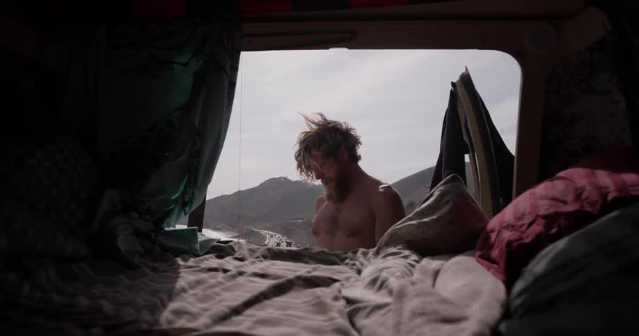 A man taking off his shirt behind a van