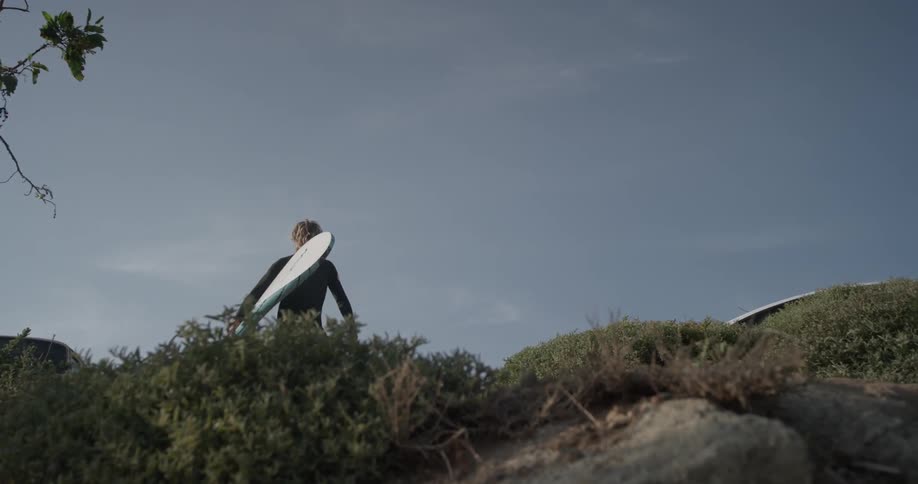A man is walking while holding a surfboard