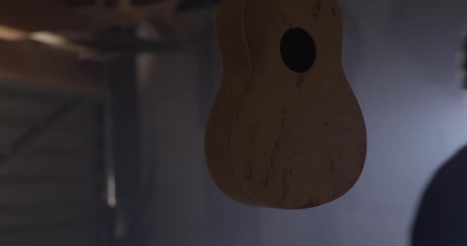 A young man walks past an incomplete ukulele in a dark workshop