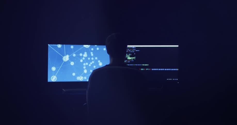 Man sitting at computer desk watching two monitors