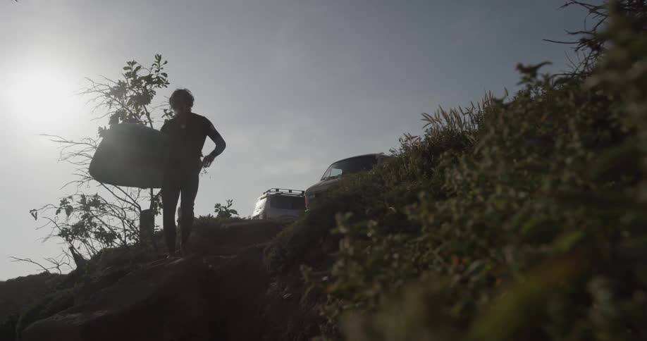 A man carrying a surfboard down a hill