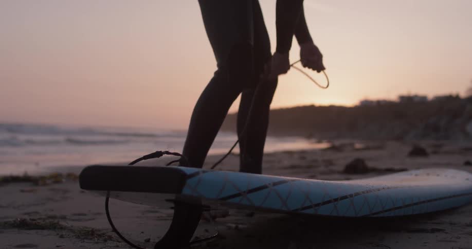 A surfer walks along the beach towards his board then he picks the board up