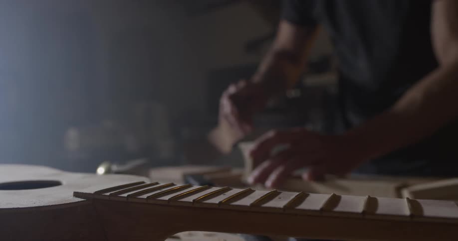 Man sands a piece of wood to make a guitar