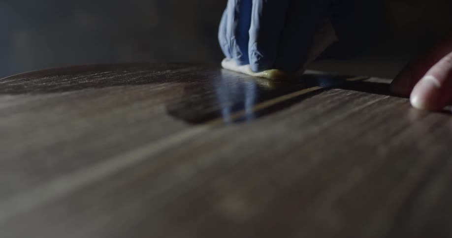 A person polishes a piece of dark wood while wearing a latex glove