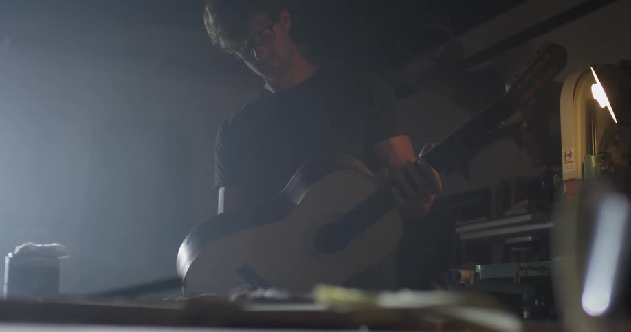 A man that is picking up a guitar and looking closely at it