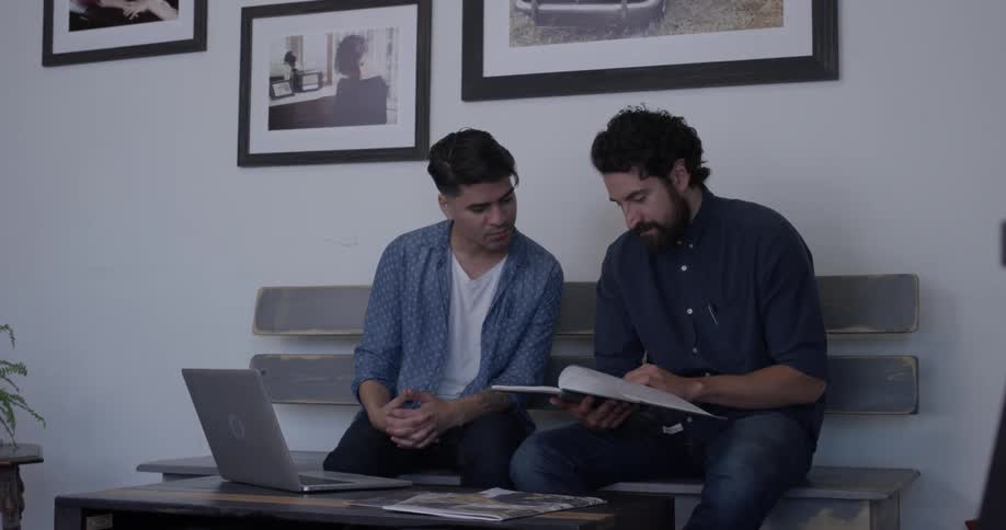 Two men sitting on a bench reading a book together