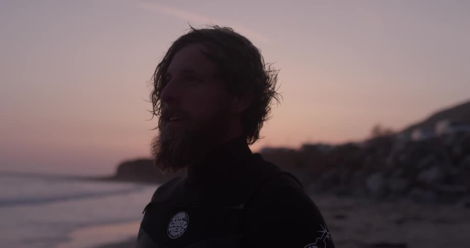 A man standing next to the ocean at sunset