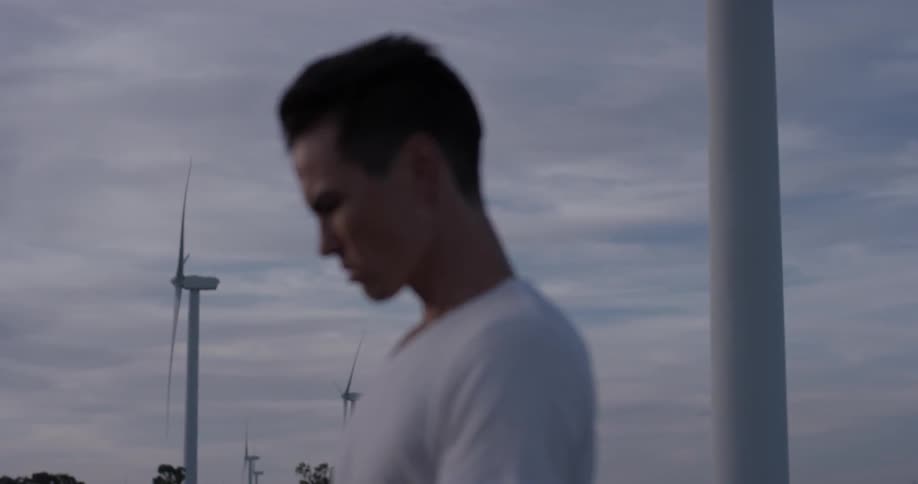 A man that is looking down at a tablet near some windmills