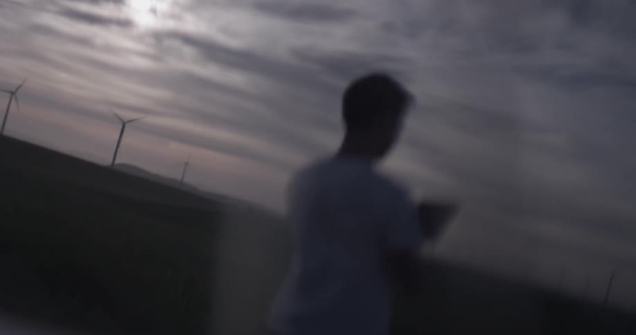 A man is reflected on a car as he is on his tablet in a field of wind turbines