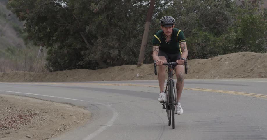 A man is riding a bicycle up a curved road