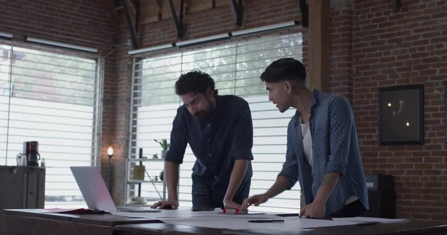 Two men in an office having a discussion while working on a laptop