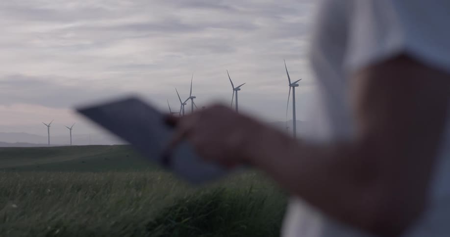 A man uses a tablet in a field of windmills that are generating electricity