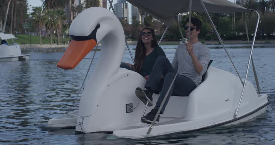 A man and woman that are pedaling a swan boat together