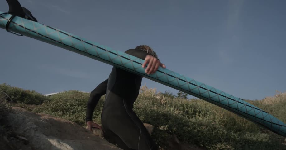 Man carrying a surfboard while climbing down rocks