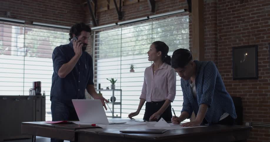 Three people discuss things around a table, one is on the phone while the others are writing on paper