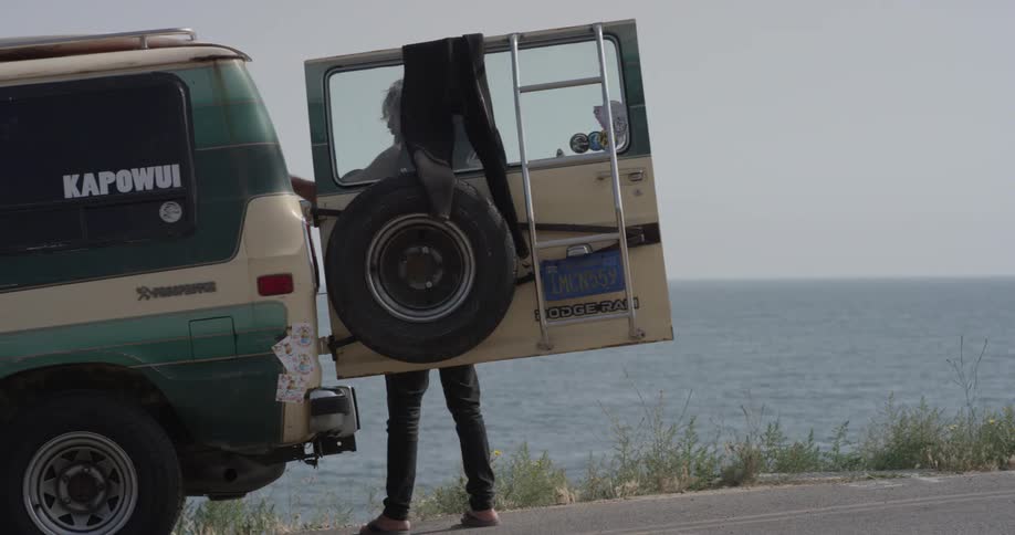 A man getting a surfboard out of the back of a car