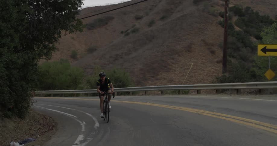 Man riding a bike up a hill on an empty road