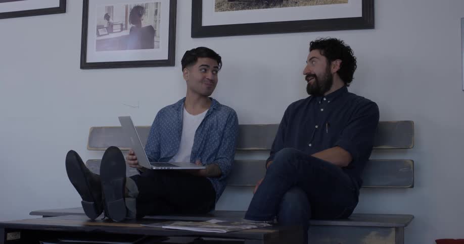 Two men sitting on a bench looking at a laptop