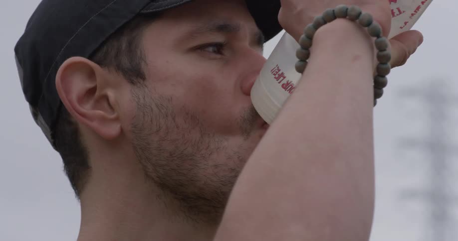 A man looks into the distance as he takes a drink from a water bottle