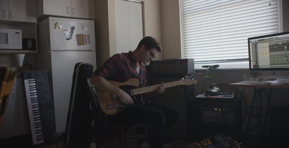 A man sitting in a kitchen area playing a guitar