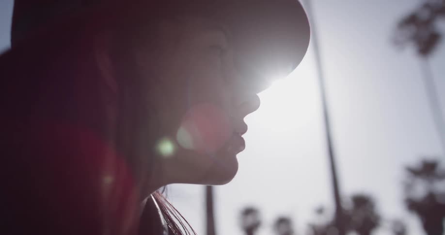 The camera pans around a woman's face as the stares off into the distance with the sun behind her