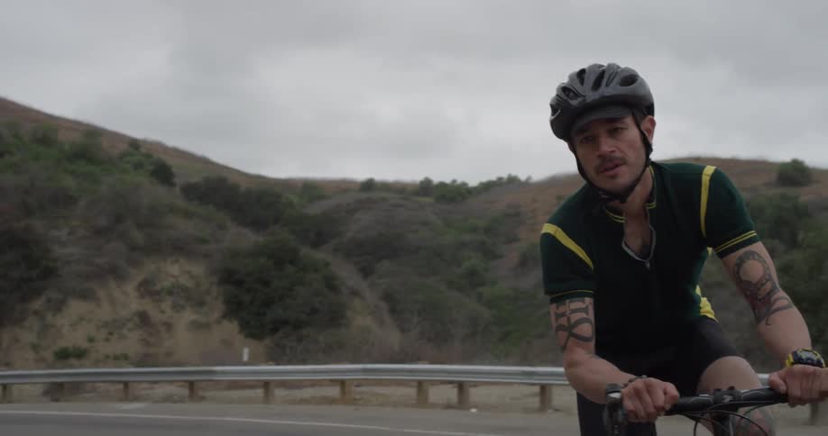 Man riding a bike on an empty road surrounded by hills